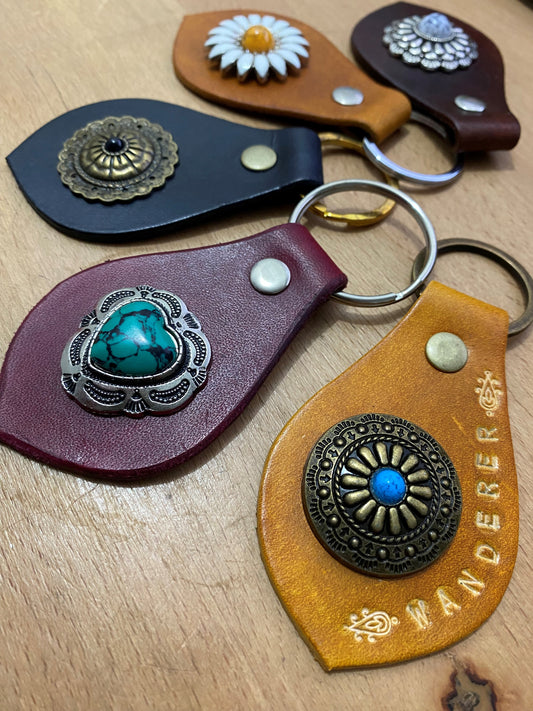 Image of five Leather keytags dyed in various colours with large decorative silver and bronze embellishments.